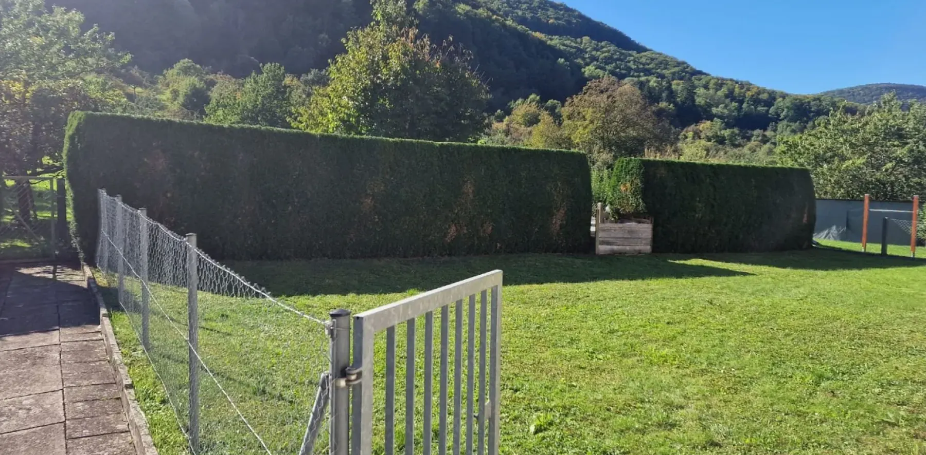 Frisch geschnittene Hecke und gemähter Rasen vor bewaldeten Hügeln